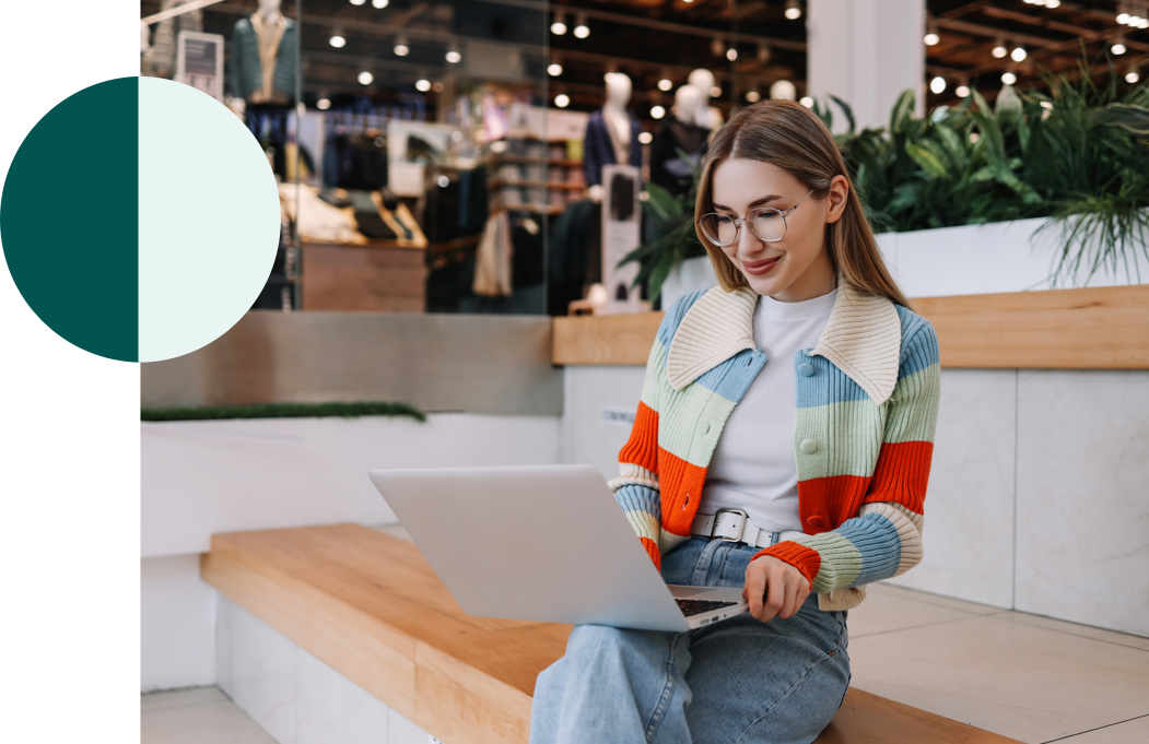 Woman sitting on a bench in a shopping mall on a laptop.